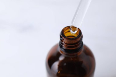 Işık arka planında pipetten şişeye serum damlatıyor, yakın plan. Metin için boşluk