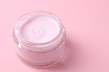 Pembe arka planda bir kavanoz nemlendirici krem, yakın plan. Metin için boşluk