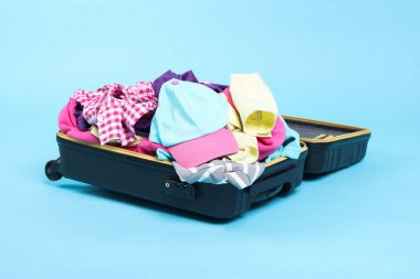 Açık mavi arka planda giysilerle dolu bavul.