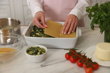 İçerideki mermer masada ıspanaklı lazanya yapan kadın, yakın plan.