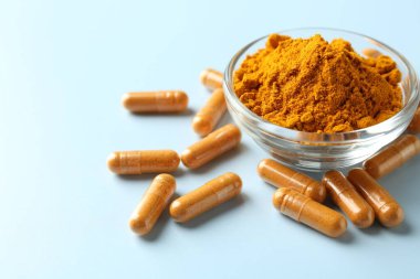 Açık mavi arka planda zerdeçal kapsülleri ve toz, yakın plan. Metin için boşluk