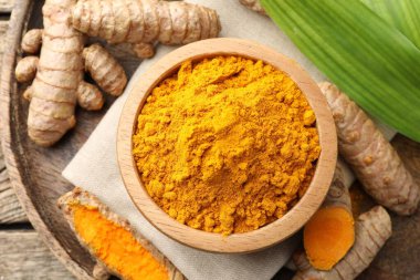 Tabaktaki zerdeçal tozu, kökler ve yapraklar ahşap masada, düz yerde.