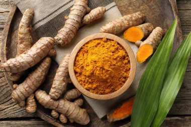 Turmeric powder in bowl, roots and leaves on wooden table, flat lay clipart