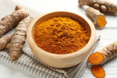 Aromatik zerdeçal tozu ve beyaz ahşap masa üzerinde taze kökler, yakın plan.