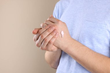 Bej arka planda el kremi süren bir adam, yakın plan. Metin için boşluk