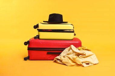 Sarı arka planda şapkalı ve dağınık elbiseli bavullar.