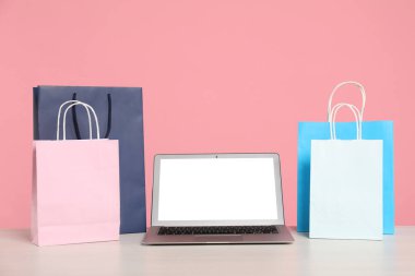 İnternet alışverişi. Laptop ve renkli kese kağıtları pembe arka planda.