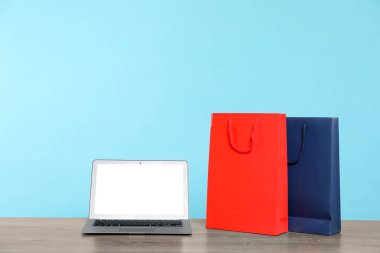 İnternet alışverişi. Diz üstü bilgisayar ve renkli kese kağıtları açık mavi arkaplana karşı ahşap masada.