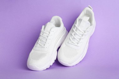 Mor arka planda bir çift şık beyaz spor ayakkabı.