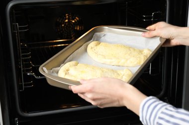 Yanmamış calzone pizzayla tabağı fırına koyan kadın, yakın plan.