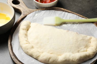 Pişmemiş calzone pizza ve yumurta sarısı gri masada, yakın plan.