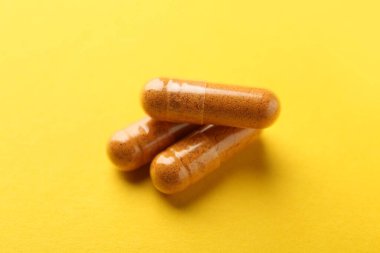 Sarı arka planda üç zerdeçal kapsülü, yakın plan.