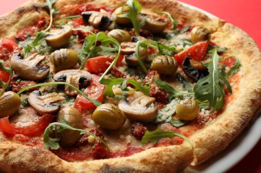 Kırmızı arka planda mantarlı, zeytinli ve roka aromalı lezzetli pizza.