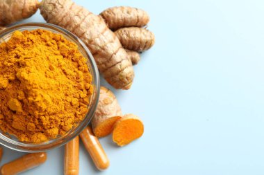 Açık mavi zemin üzerinde zerdeçal kapsülleri, toz ve kökler, düz zemin. Metin için boşluk