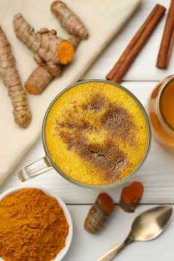 Bardaktaki lezzetli zerdeçal latte ve beyaz ahşap masa üzerindeki malzemeler.