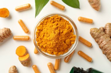 Beyaz zemin üzerinde zerdeçal kapsülleri, toz, kökler ve yeşil yapraklar düz yatar