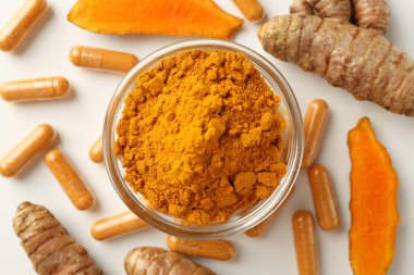 Beyaz zemin üzerinde zerdeçal kapsülleri, toz ve kökler düz yatıyordu