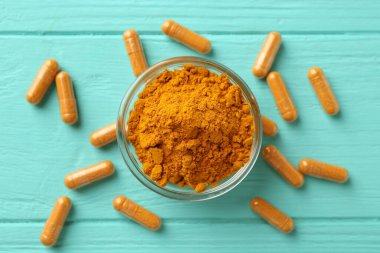 Turkuaz ahşap masa üzerinde zerdeçal kapsülleri ve pudra düz yerde.