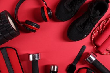 Farklı spor aletleri, kol saati ve kırmızı arka planda kulaklıklar, düz yatış. Metin için boşluk