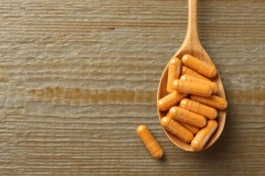 Tahta masada kaşık içinde zerdeçal kapsülleri, üst manzara. Metin için boşluk