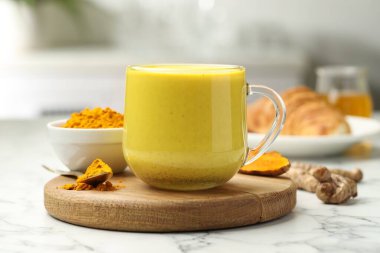 Delicious turmeric latte, powder and rhizomes on white marble table, closeup clipart