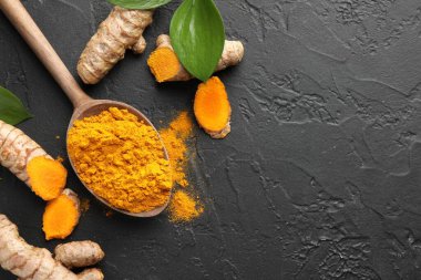 Kaşıkta aromatik zerdeçal tozu, taze kökler ve siyah masa üzerindeki yapraklar, düz yatış. Metin için boşluk