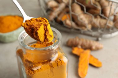 Masadaki cam kavanozdan kaşık aromatik zerdeçal tozu alarak, yakın plan.