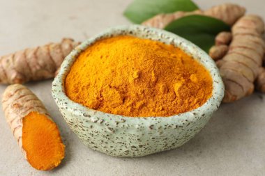 Kasede Aromatik zerdeçal tozu, taze kökler ve açık gri masadaki yapraklar, yakın plan.