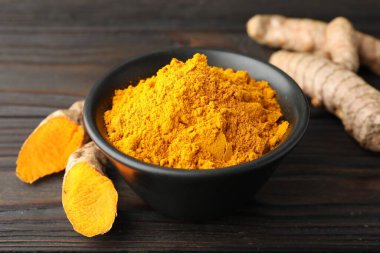 Kasede Aromatik zerdeçal tozu ve ahşap masada taze kökler, yakın plan.