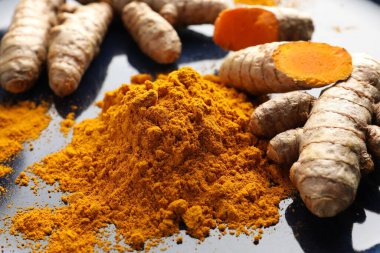 Aromatik zerdeçal tozu ve mavi tabakta taze kökler, yakın plan.