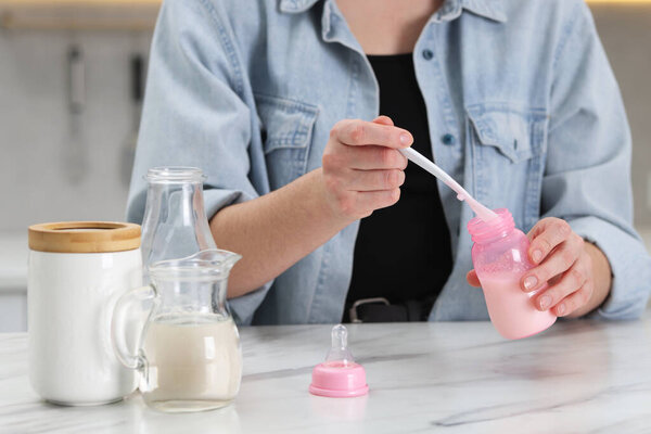 Mother making baby formula in feeding bottle at table indoors, closeup