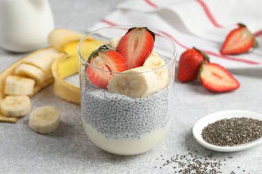 Çilekli lezzetli chia pudingi ve açık gri masada muz, yakın plan.