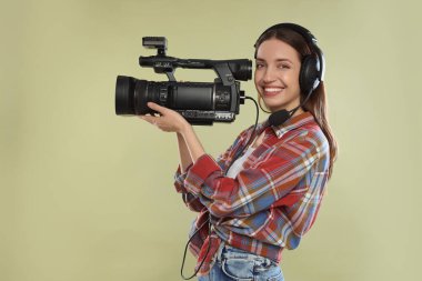Profesyonel video kamerası ve soluk zeytinli kulaklığı olan mutlu kadın.