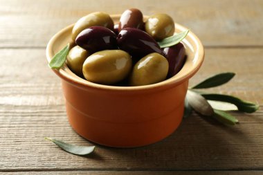 Lezzetli zeytinler ve yapraklar ahşap masada, yakın plan