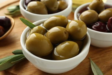 Lezzetli zeytinler tabakta ve yeşil yapraklar masada, yakın plan.