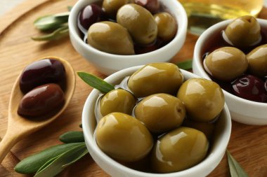 Lezzetli marine edilmiş zeytin kaseleri, kaşık ve yeşil yapraklar ahşap tahtada, yakın plan.