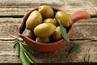 Salamura edilmiş lezzetli zeytinler ve ahşap masada yeşil yapraklar, yakın plan.