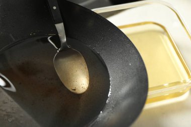 Beyaz masadaki tavada kullanılmış yemek yağı ve kaşık, yakın plan.