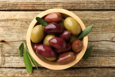 Lezzetli marine edilmiş zeytinler kasede ve ahşap masada yeşil yapraklar, üst manzara.