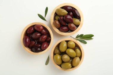 Lezzetli zeytinler tabakta ve yapraklar beyaz masada, düz yerde