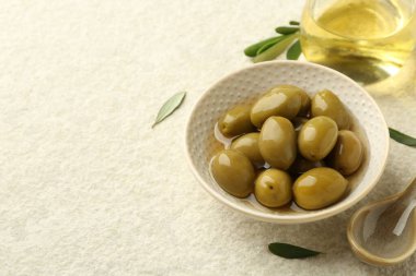 Lezzetli yeşil zeytinler kasede, yapraklar ve yağlar bej masada, yakın plan. Metin için boşluk