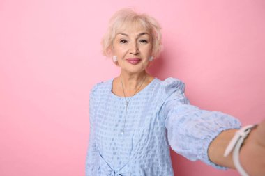 Zarif büyükanne pembe arka planda selfie çekiyor.