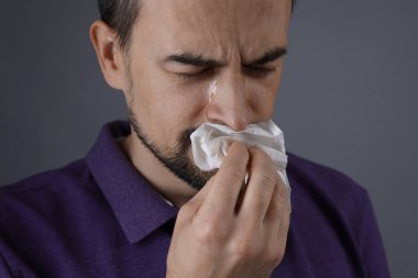 Gri arka planda ağlayan kağıt mendilli üzgün adam.