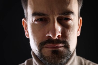 Sad man crying on black background, closeup