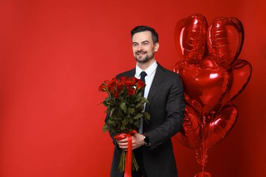 Sevgililer Günün kutlu olsun. Kalp şeklinde balonları ve kırmızı arka planda gül buketi olan yakışıklı bir adam. Metin için boşluk