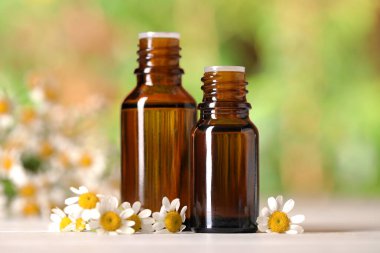 Beyaz ahşap masada, bulanık arka planda, yakın planda, gerekli yağ ve papatya çiçekleri.