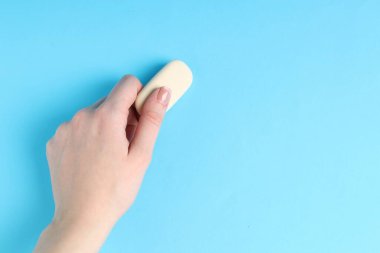 Açık mavi arka planda silgi kullanan bir kadın, yakın plan. Metin için boşluk