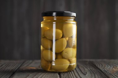 Cam kavanozda yeşil zeytin turşusu. Ahşap masada, gri arka planda.