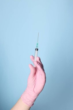 Tozlu açık mavi arka planda ilaçlı şırınga tutan doktor, yakın plan.
