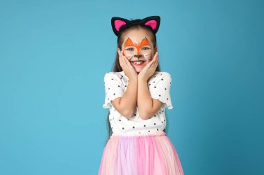 Yüzü ve kulakları açık mavi arka plandaki kedi gibi boyalı tatlı bir kız.